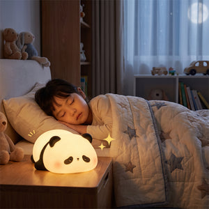 A small panda-shaped night light glowing softly on an open book, with a hand holding the book in a dimly lit room.