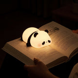 A small panda-shaped night light glowing softly on an open book, with a hand holding the book in a dimly lit room.